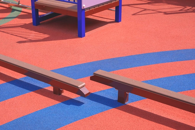 Kids Balance beams on colorful orange and blue rubber floor in public outdoors playground area