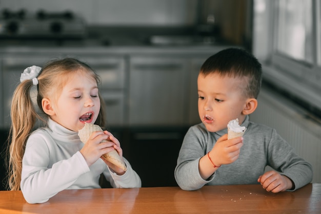 キッチンでアイスクリームコーンを食べる子供たちの男の子と女の子はとても楽しいとても甘いです