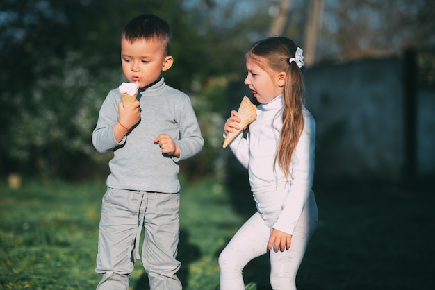 Kids Boy and girl eating ice cream outdoors on grass and trees background very sweet