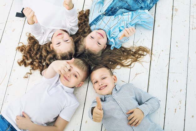 Дети мальчики и девочки веселые, счастливые красивые лежат на белом деревянном полу и улыбаются