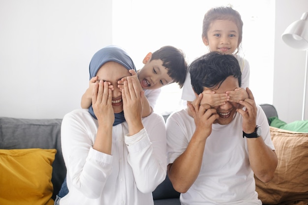 Kids closing eyes of parents using hands giving surprise Family bonding at home