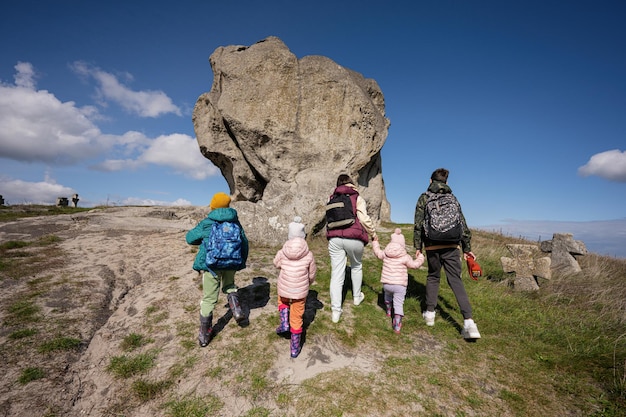 Kids exploring nature Children wear backpack hiking with mother near big stone in hill Pidkamin Ukraine