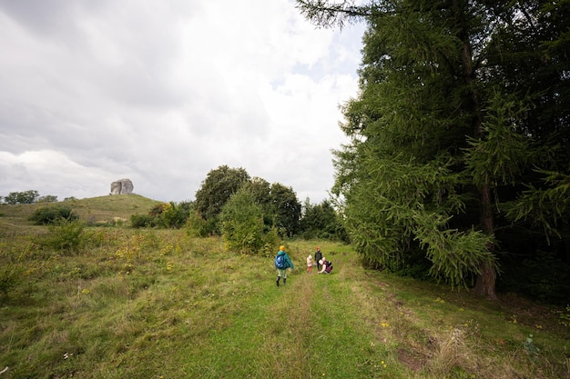 Kids exploring nature Children wear backpack hiking with mother near big stone in hill Pidkamin Ukraine