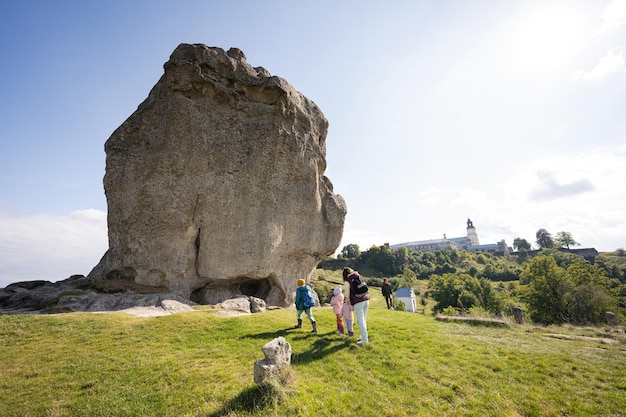 Kids exploring nature Children wear backpack hiking with mother near big stone in hill Pidkamin Ukraine