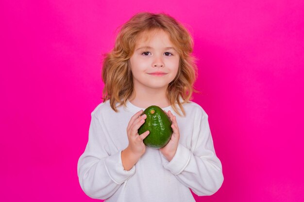 Kids face with fruits Kid hold red avocado in studio Studio portrait of cute child with avocado isolated on pink background