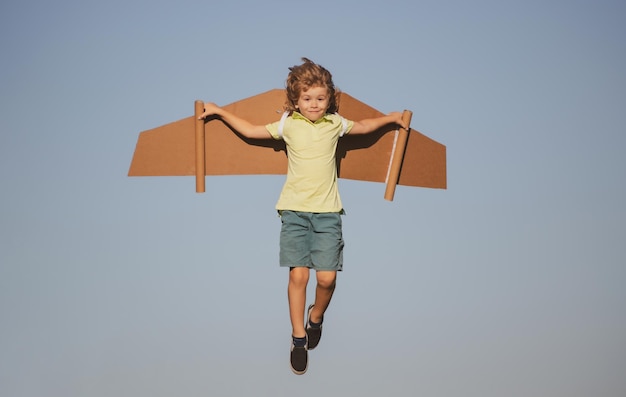 I bambini volano divertente bambino ragazzo pilota che vola con le ali di aeroplano di cartone giocattolo sull'inizio dello spazio della copia del cielo blu