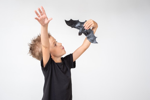 Kids Halloween A beautiful emotional boy in a black Tshirt holds a bat toy on a white studio background The boy scares