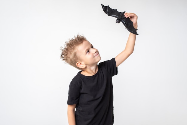 Kids halloween een mooie emotionele jongen in een zwart t-shirt houdt een vleermuisspeelgoed vast op een witte studioachtergrond de jongen schrikt