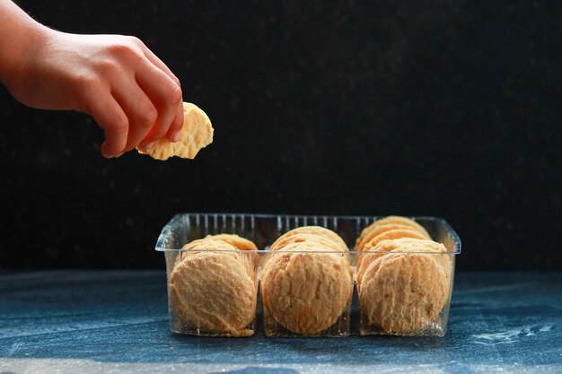 子供の手は暗い背景の箱からクッキーを取ります