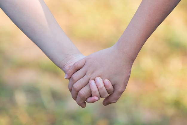 kids' hands holding for support and friendship, blur green grass background