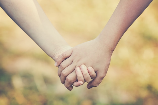 Foto le mani dei bambini che tengono per il supporto e l'amicizia, offuscano il fondo dell'erba verde