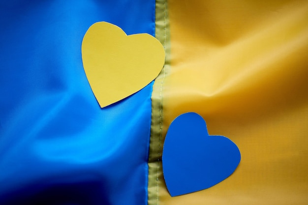 写真 ウクライナの旗の背景にyellowbluepaperheartsを保持している子供の手