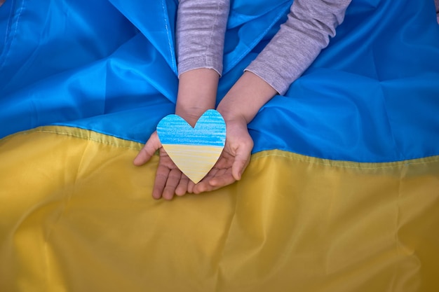 写真 ウクライナの旗の背景にyellowbluepaperheartsを保持している子供の手