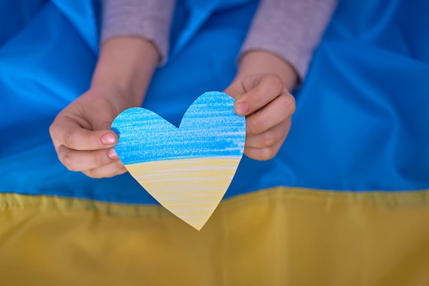 Mani dei bambini che tengono cuori di carta gialli blu sullo sfondo della bandiera ucraina