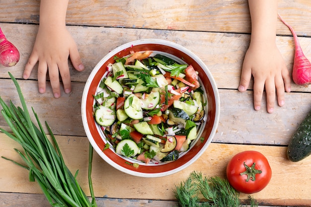 Kids hands preparing fresh healthy salad near variety of vegetables and fruits on wooden table, flat lay
