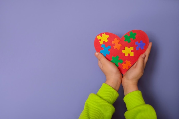 Kids hands with a red heart with pieces of colored puzzles inside