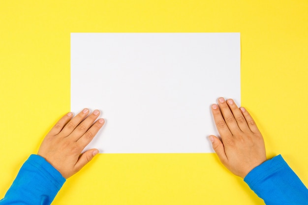 Kids hands with white blank paper card on yellow background