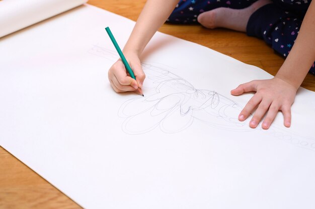 사진 아이들은 취미. 어린 아이 소녀는 집에서 바닥에 앉아 종이에 연필로 그립니다.