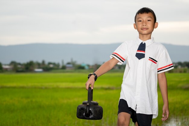 Kids holding old hot water pot on blurred rice field and sky 