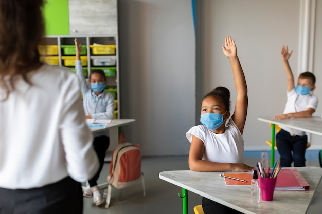 Foto bambini che tengono le mani in alto per rispondere in classe