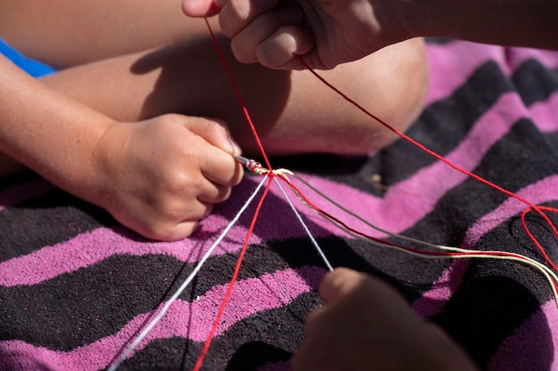 Photo kids knotting multicolored cotton yarn strings to make a bracelet
