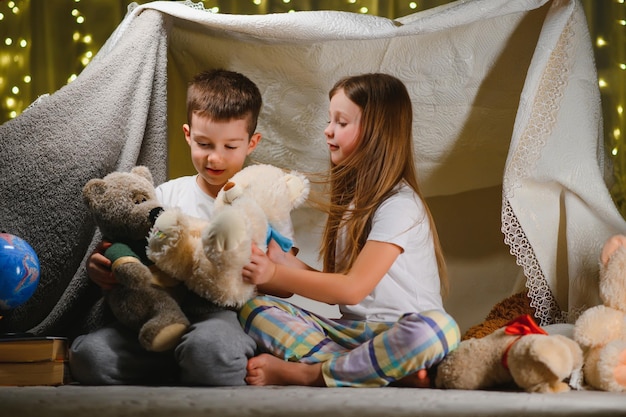 Kids lying on floor in cozy nursery Boy and girl holding flashlights in hands Children play in a makeshift tent in the nursery