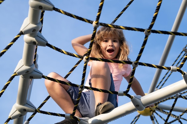 Kids play and climb outdoors on sunny summer day Child boy climbed on top of the rope web on playground Kid boy climbing the net