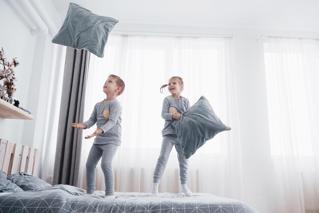 Photo kids playing in parents bed children wake up in sunny white bedroom boy and girl play in matching pajamas sleepwear and bedding for child and baby nursery interior for toddler kid family morning