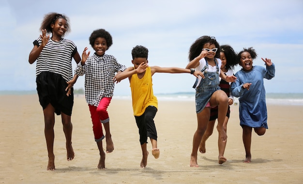 ビーチで砂の上を走って遊んでいる子供たち、夏にビーチで手をつないでいる子供たちのグループ、海と青い空を背景にした背面図