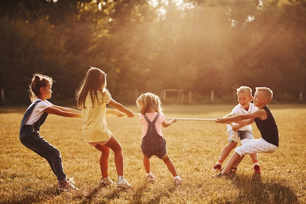 Kids playing tug of war game in the beautiful meadow at sunny day.