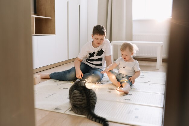 Kids playing with a cat at home brother and little sister having fun together