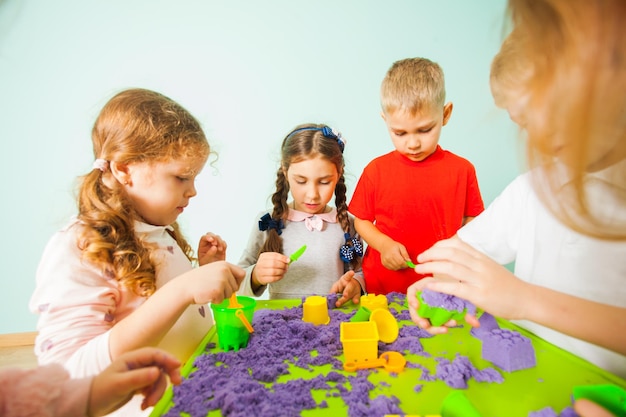 Kids playing with color kinetic sand at table at home