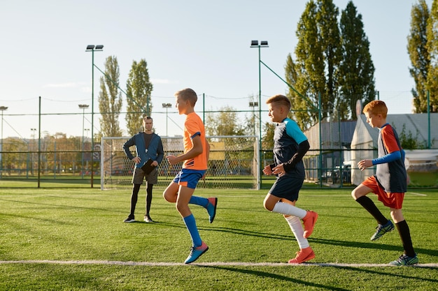 축구 코치의 통제하에 잔디밭에서 축구를 연습하는 아이들. 경기장에서 운동하는 어린 소년들의 그룹
