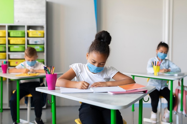 Photo kids protecting themselves with face masks in classroom