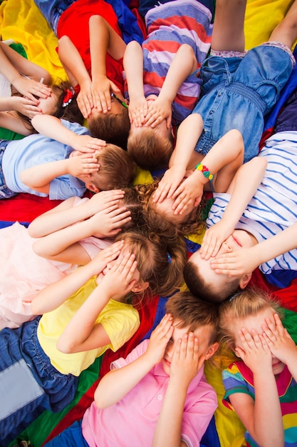 Kids relaxing on a floor while break laying covering faces with their hands Children working on relaxation techniques Summer daycamp Danger of pediculosis when childrens head are too close