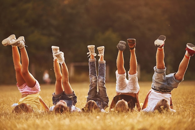 Foto bambini che riposano insieme nel campo durante il giorno pieno di sole. alzare le gambe.