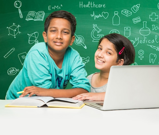 Kids and science concept - cute indian little kid student or scientist studying science or experimenting with microscope and Chemicals with diagrams doodles drawn over green chalkboard