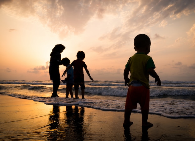 Siluette dei bambini che hanno tempo felice sulla spiaggia del mare vicino al tramonto