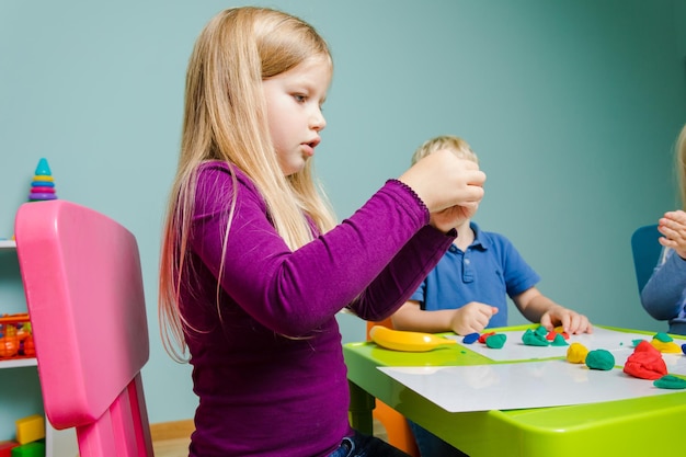 The kids sit at the desk and molding clay in the playroom