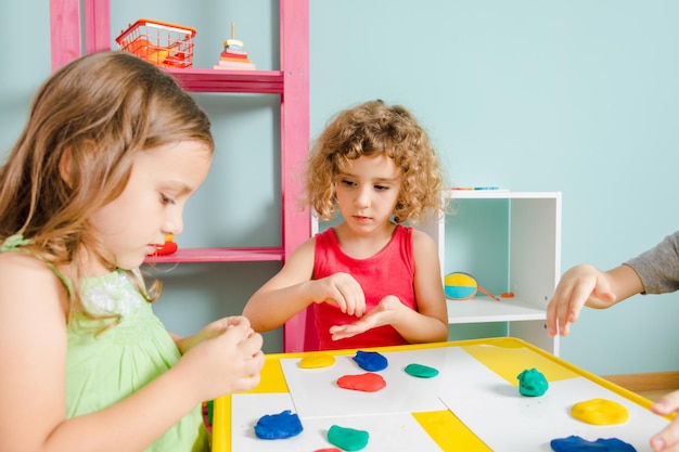 The kids sit at the desk and molding clay in the playroom