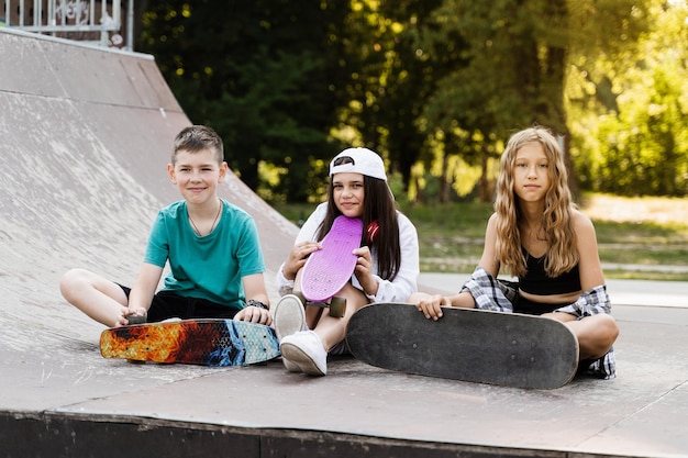 Kids smile and laugh and have fun together Children with skateboard and penny boards communicate and discuss on the sports playground Boy and girls friendship concept