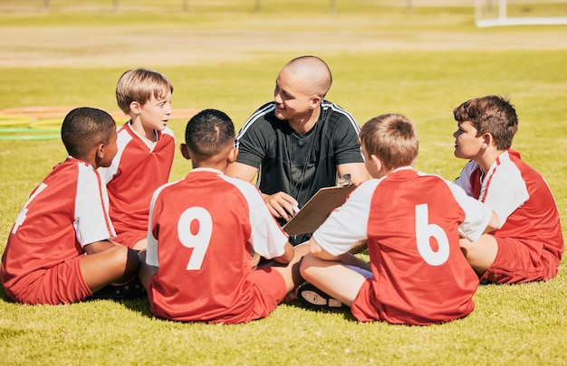 Photo kids soccer and team coach planning training with clipboard on soccer field for sport competitiion together athlete children teamwork and sit on grass before football match or workout outdoors