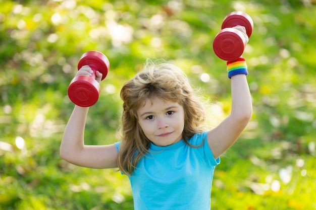 Kids sport boy is doing exercises to develop muscles child is doing exercises with dumbbells in park