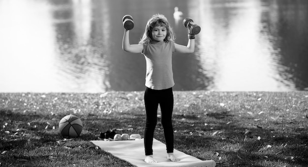 Дети занимаются спортом здоровый мальчик с гантелью упражнения на открытом воздухе маленький ребенок практикует упражнения с гантелью