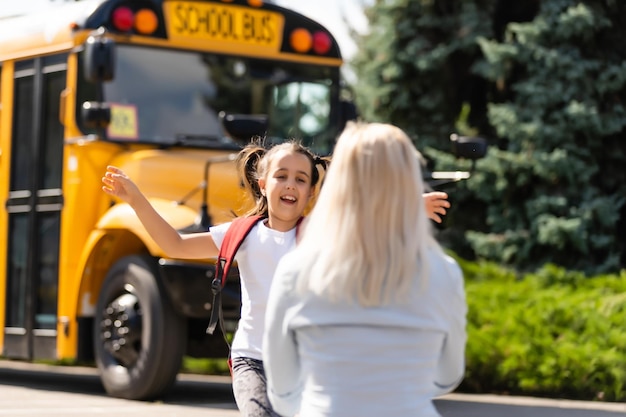 Дети-студенты бегут к матери, чтобы обнять ее после возвращения в школу возле школьного автобуса