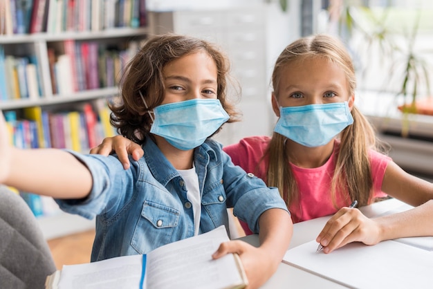 Photo kids taking a selfie in the library while wearing medical masks