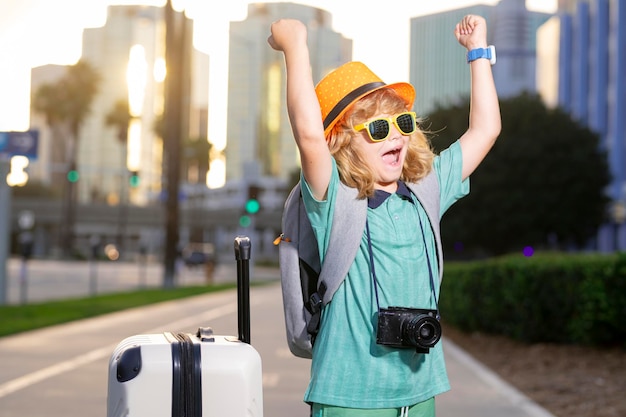 Kids travel Happy child boy carrying travel suitcases outdoor on city street Travel lifestyle and dreams of travel