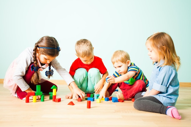 幼稚園の木の床に座っているカラフルなブロックで、さまざまな年齢の子供たちが遊んでいます。幼稚園や幼稚園向けの知育玩具。