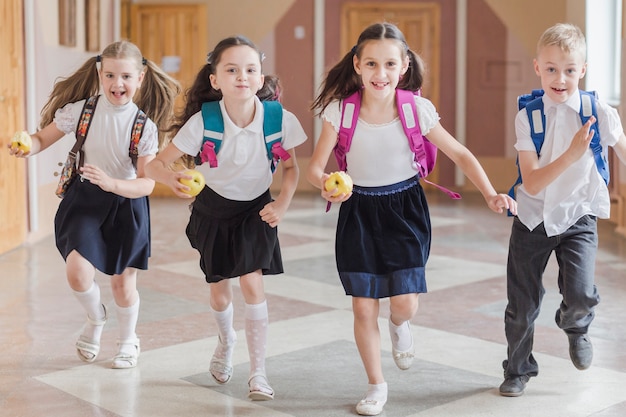 Photo kids with apples running on school corridor