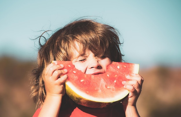 I bambini con la faccia affamata che mangiano l'anguria rossa in bocca il bambino mangia il melone